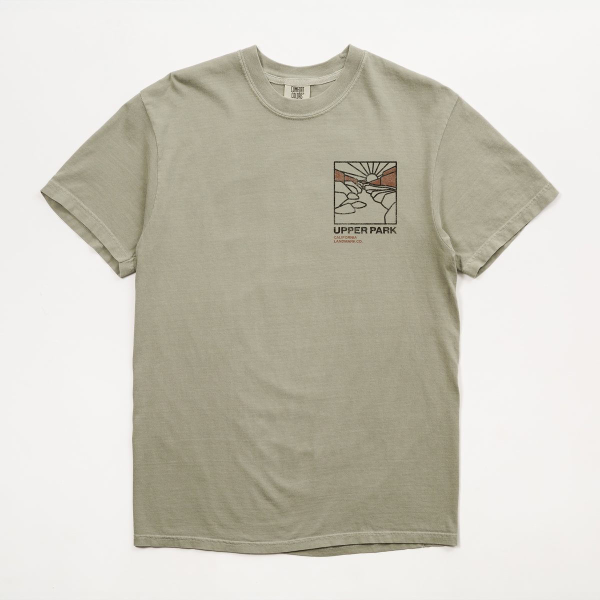 A light sage green crewneck t-shirt with a small graphic print on the left chest featuring a stylized scene and the text 'UPPER PARK california landmark co.' on a white background