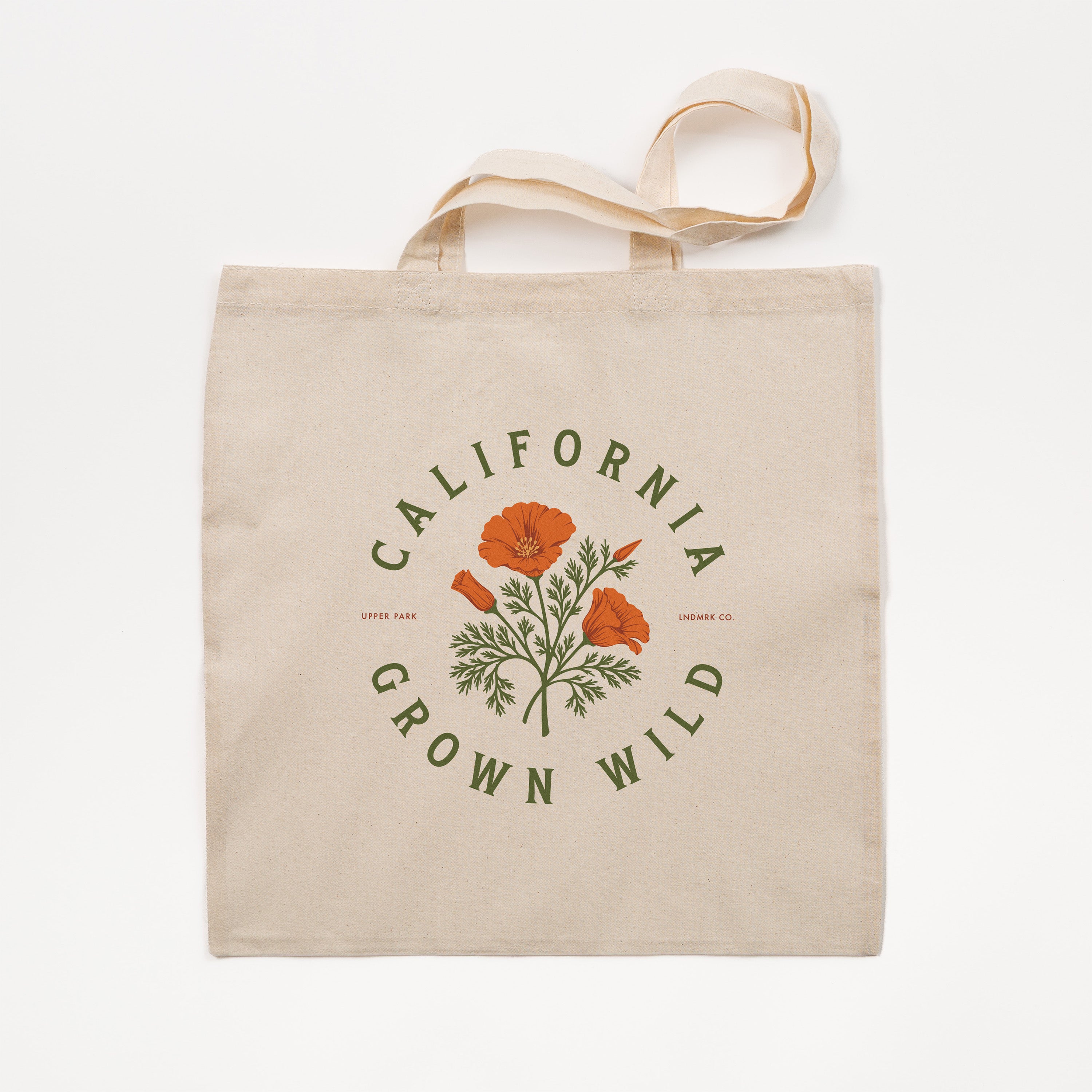 A natural canvas tote bag with a printed graphic of orange California poppies and green leaves, surrounded by the text 'CALIFORNIA GROWN WILD' in green. The bag is shown flat against a clean white background.