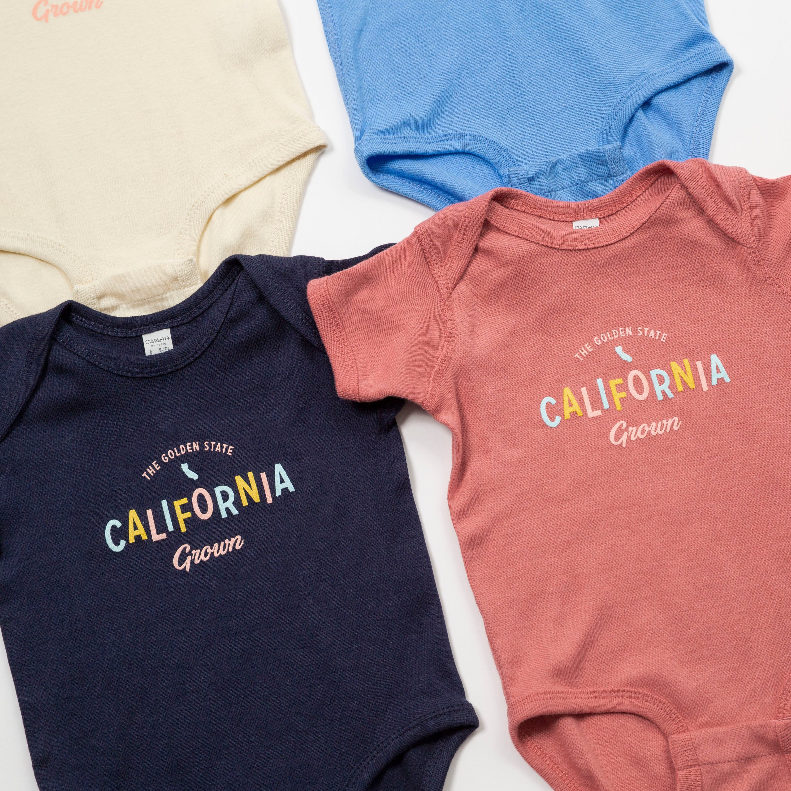 Three baby onesies in navy, blue, and pink with 'California Grown' text on a light background. - Upper Park Baby Onesie California Collection