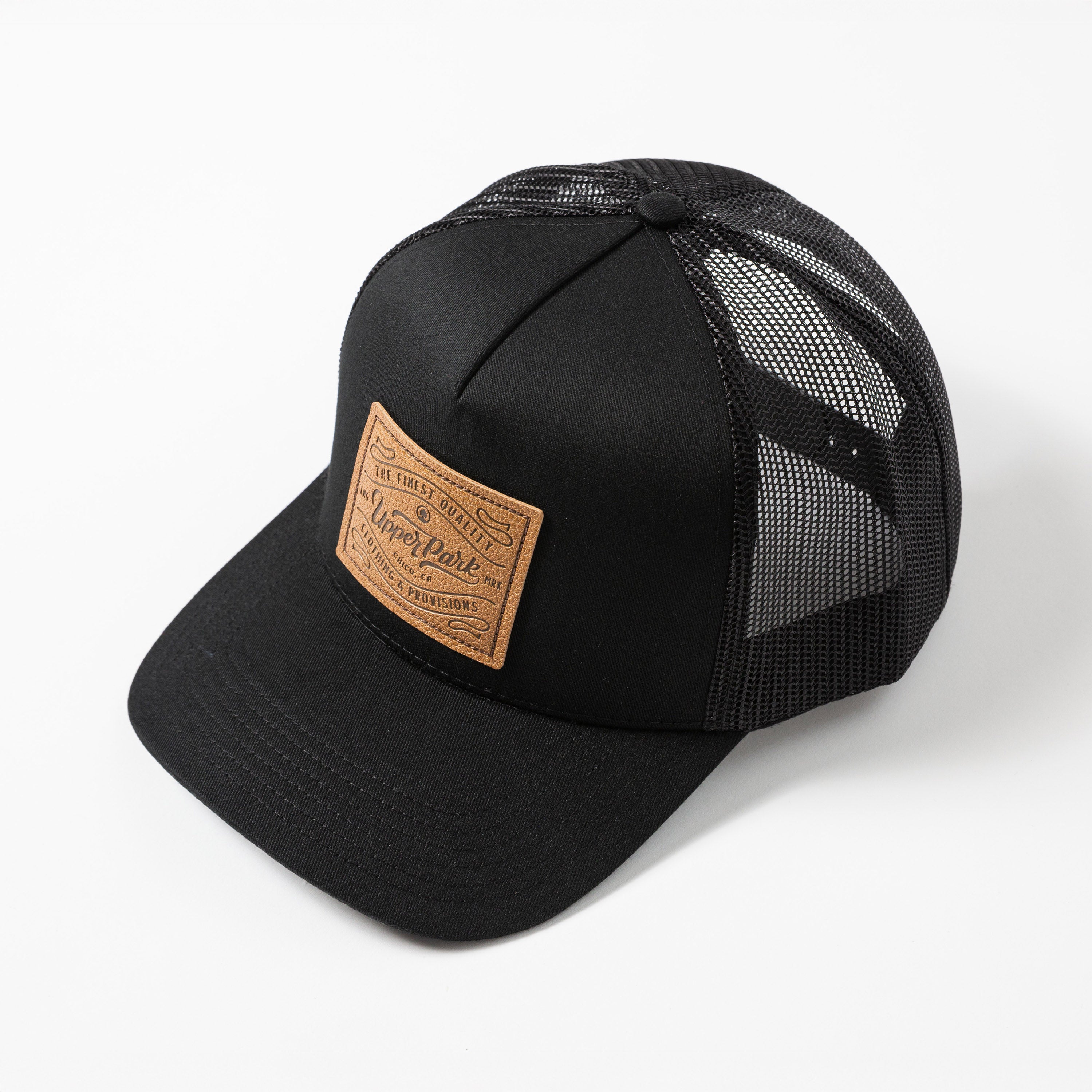 Upper Park Pro Label 5 Panel Trucker Hat - Black mesh cap with a brown leather patch on a white background