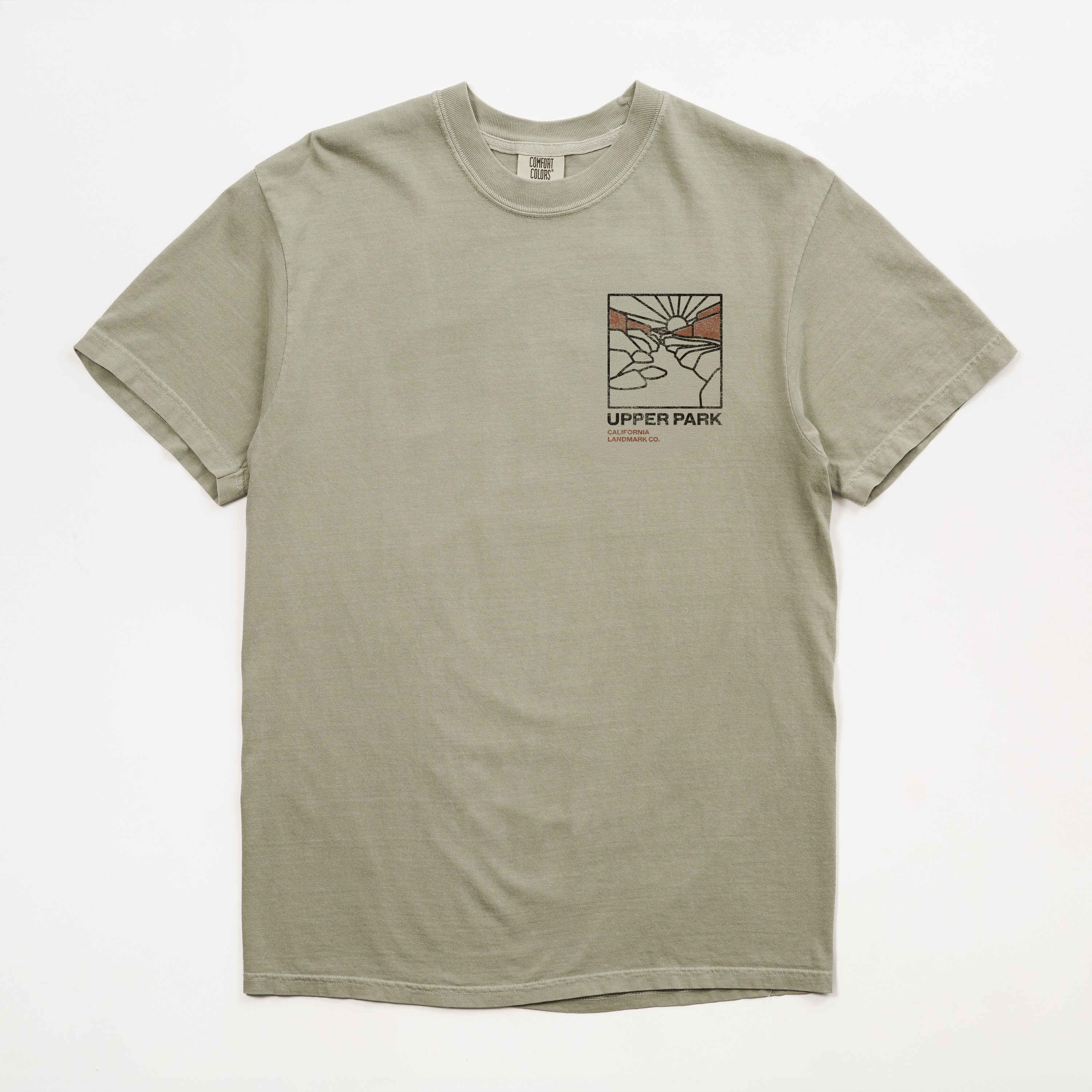A light sage green crewneck t-shirt with a small graphic print on the left chest featuring a stylized scene and the text 'UPPER PARK california landmark co.' on a white background