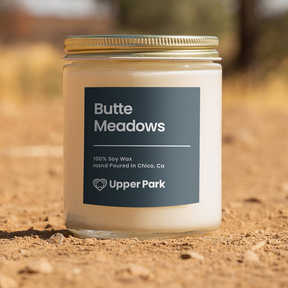 A white soy wax candle jar with a label reading 'Butte Meadows' placed on a natural outdoor background.