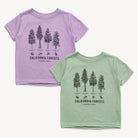 Two short-sleeve kids' t-shirts shown on a light gray background, one in light purple and one in light sage green. Both shirts feature a black line art graphic of California forest trees with the text 'CALIFORNIA FORESTS' and 'COMMON WEAR' printed below.