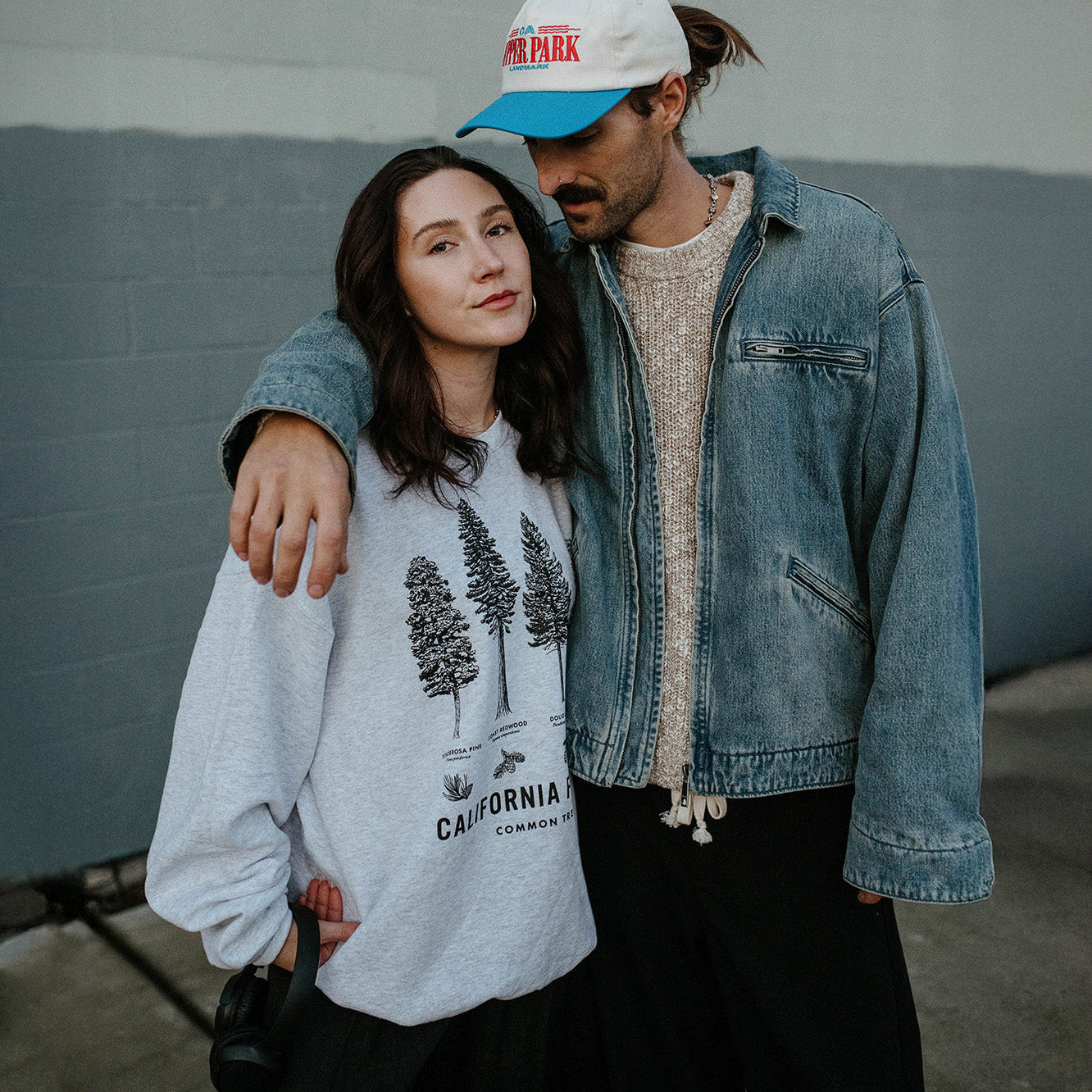 Two people standing close together against a gray wall. Upper Park - California Forests Crew Neck sweatshirt