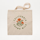 A natural canvas tote bag with a printed graphic of orange California poppies and green leaves, surrounded by the text 'CALIFORNIA GROWN WILD' in green. The bag is shown flat against a clean white background.