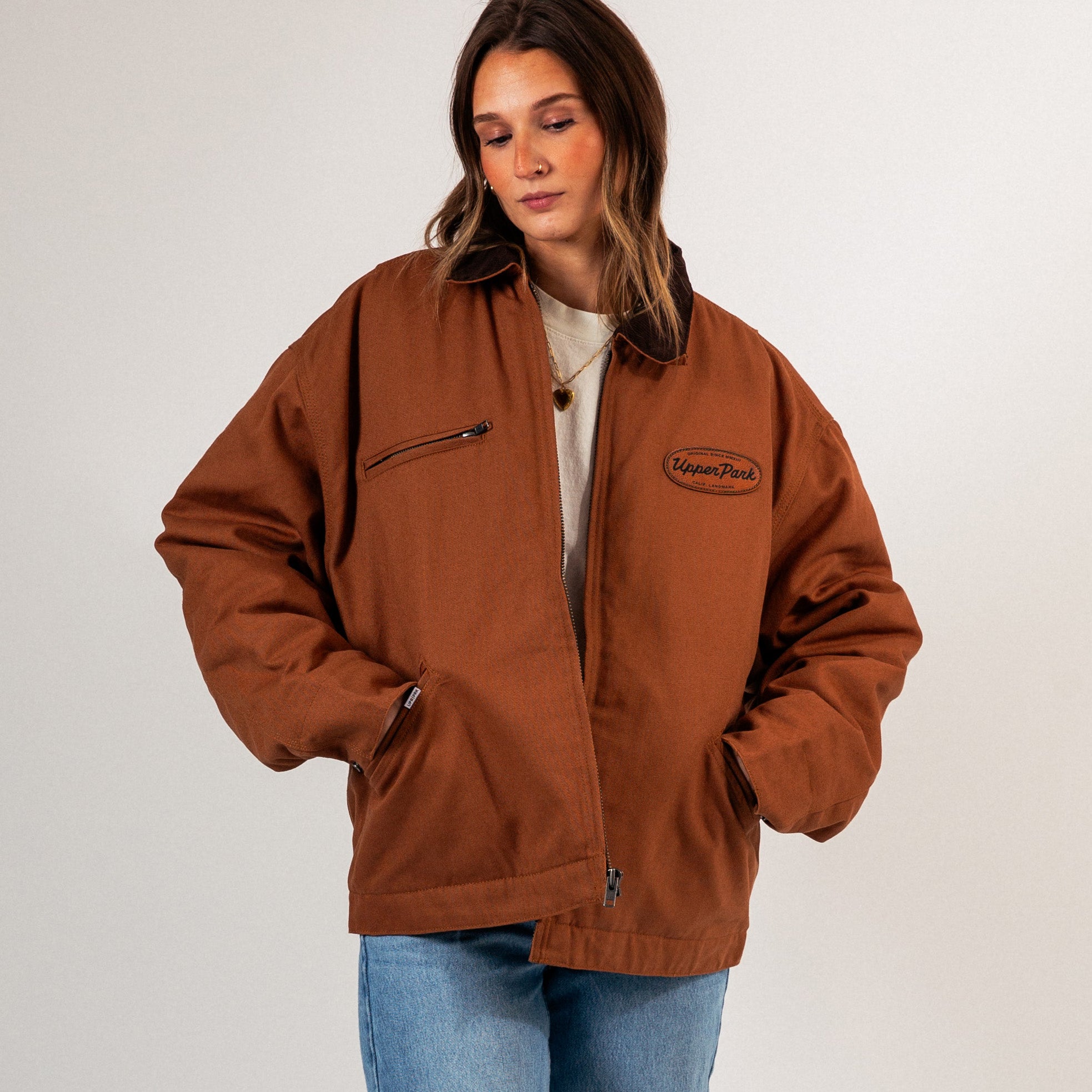 Woman wearing a brown jacket with a logo on a white background - Cultivators Upper Park Barn Jacket