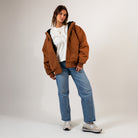 Person wearing a brown jacket, white shirt, blue jeans, and gray sneakers on a plain background - Cultivators Upper Park Duck Canvas Jacket