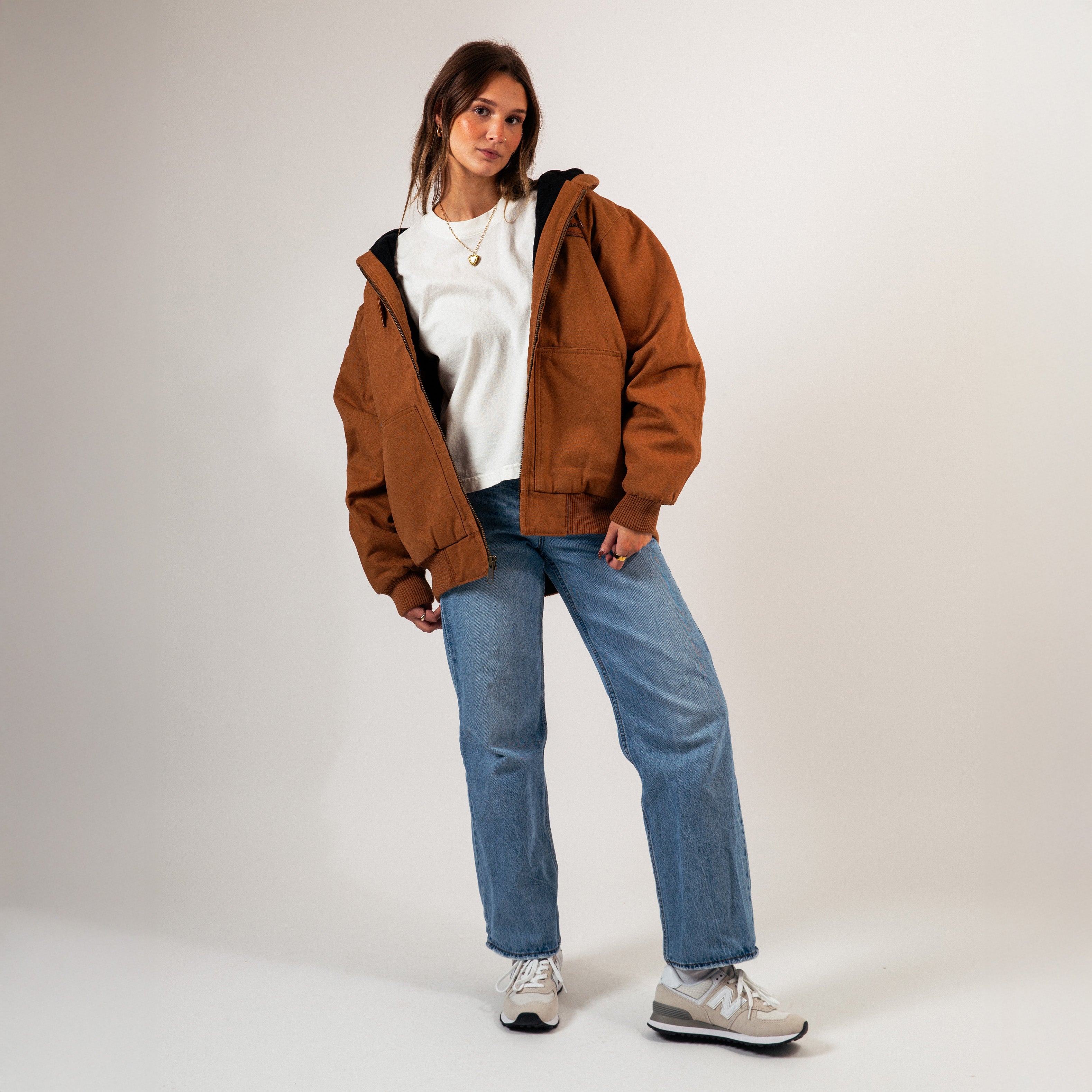 Person wearing a brown jacket, white shirt, blue jeans, and gray sneakers on a plain background - Cultivators Upper Park Duck Canvas Jacket