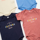 Three baby onesies in navy, blue, and pink with 'California Grown' text on a light background. - Upper Park Baby Onesie California Collection