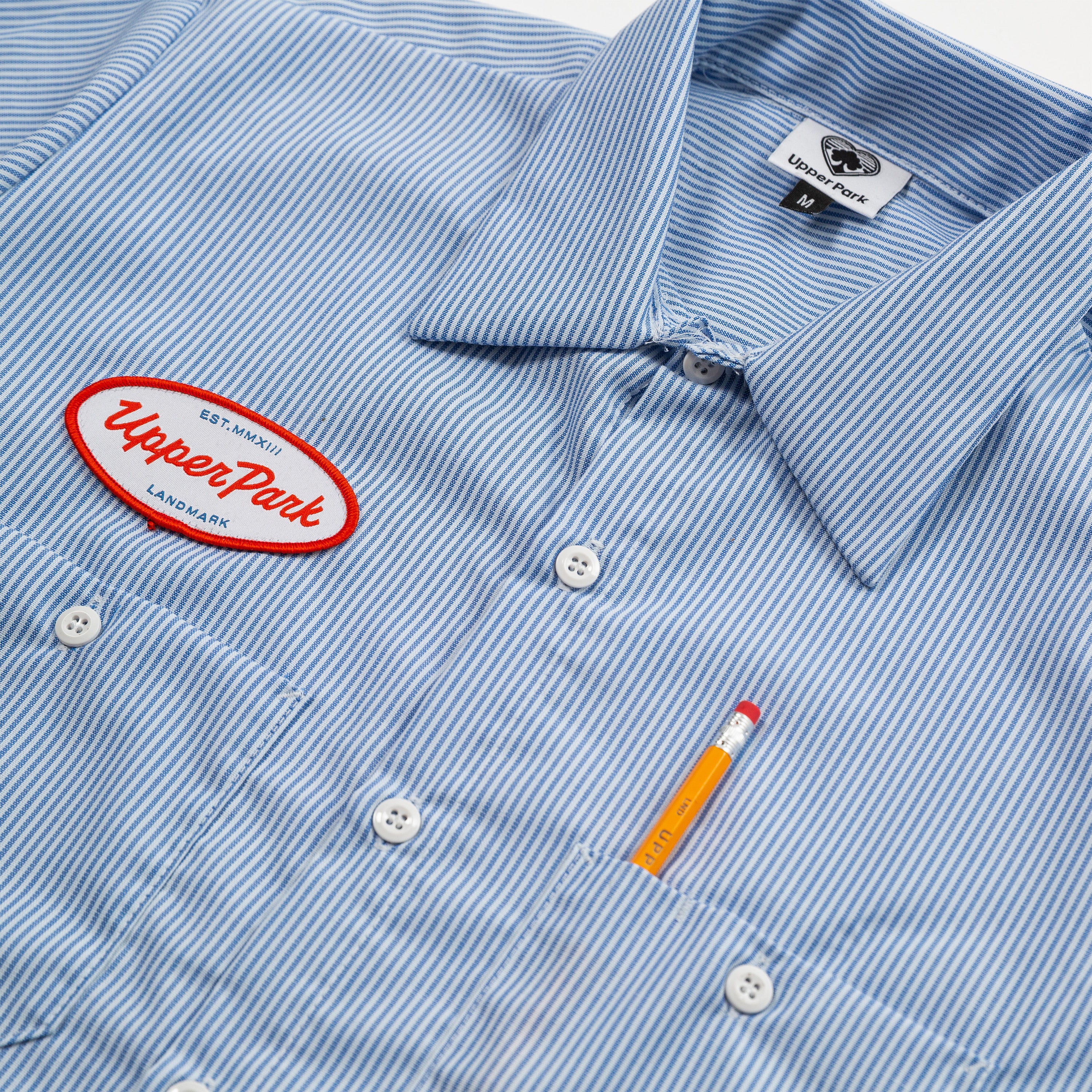 Blue striped shirt with 'Upper Park' logo and pencil detail