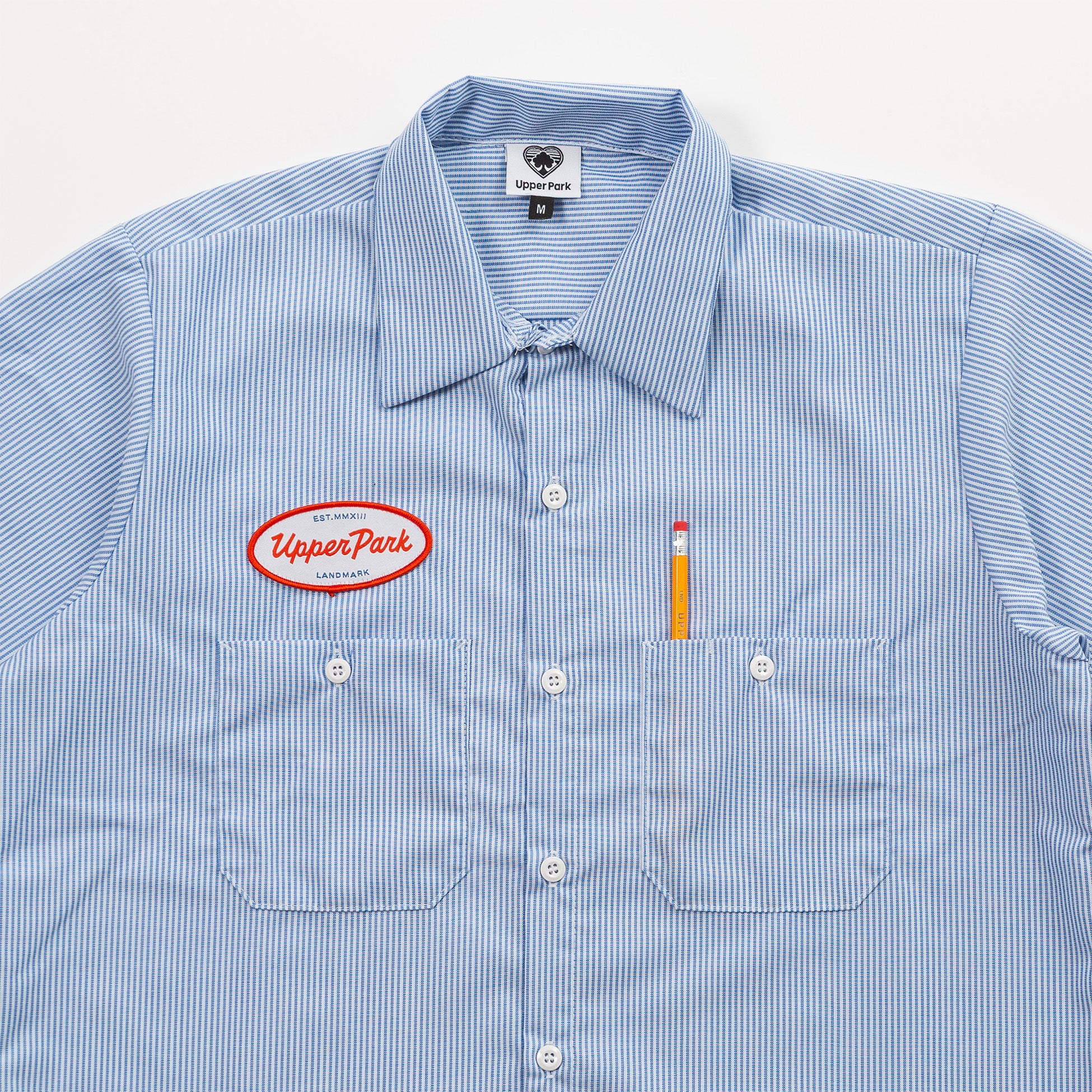 Blue striped shirt with Upper Park logo and pencil on a white background