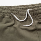 Close-up of olive green shorts with a white drawstring on a light gray background