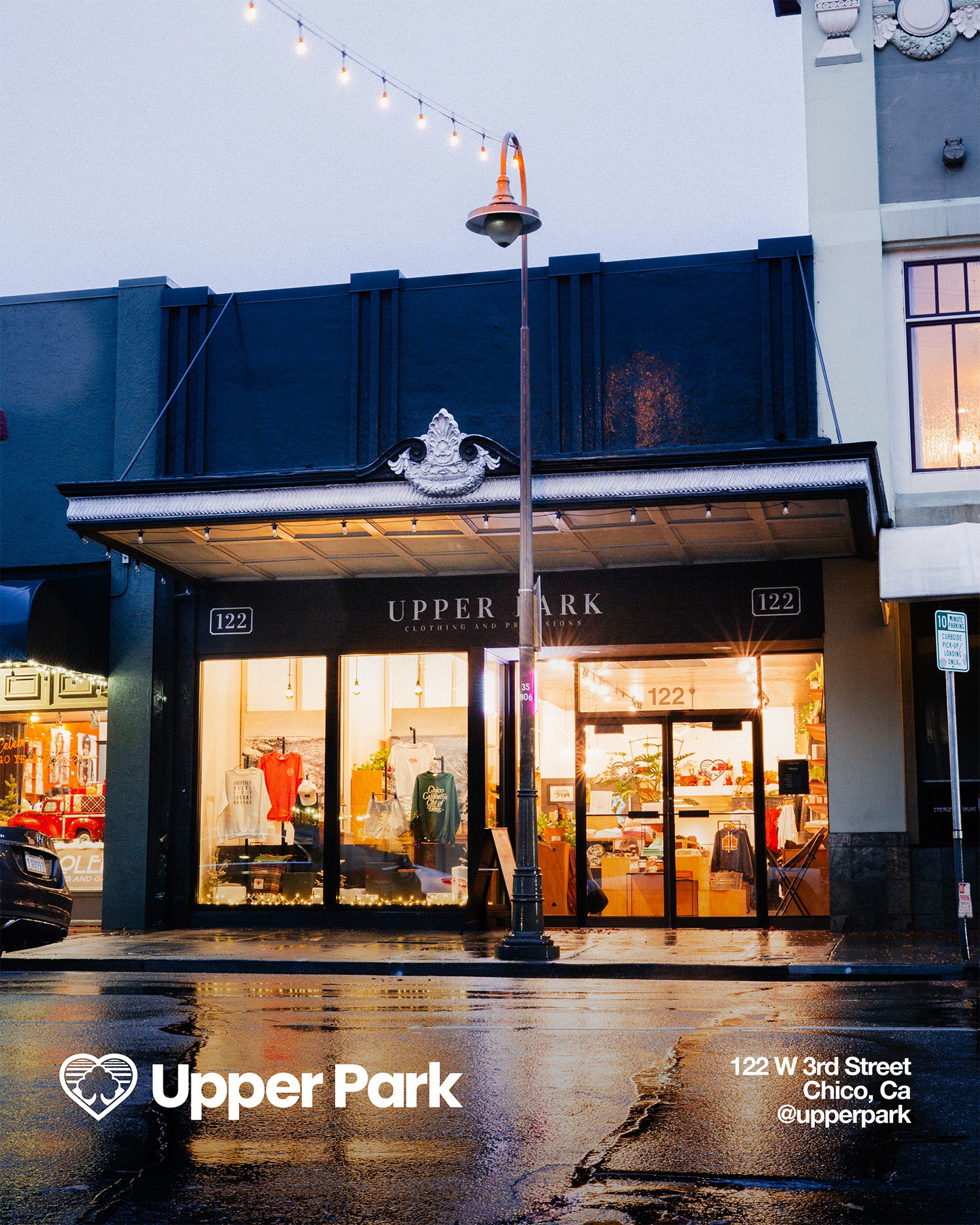 Storefront of Upper Park with illuminated windows on a wet street at dusk.