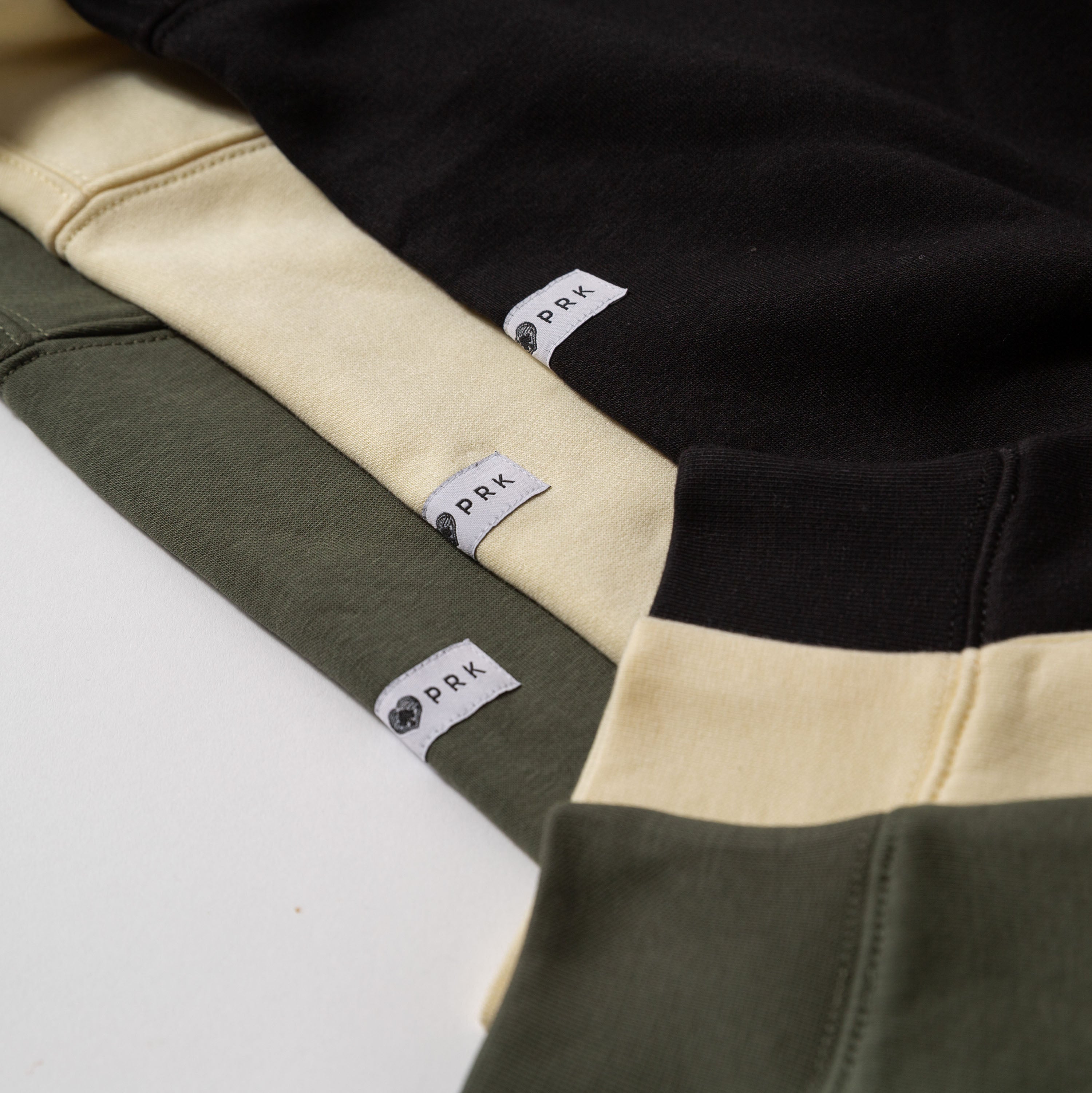 Close-up of a black, yellow, and green sweaters with Upper Park labels on a white background - Upper Park Athletics Sweater Set