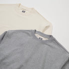 Two folded shirts, one beige and one gray, on a white background. - Basics Premium Cotton Sweater